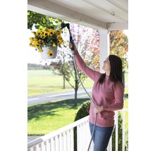 Žena zalévá visící květiny zahradní sprchou.