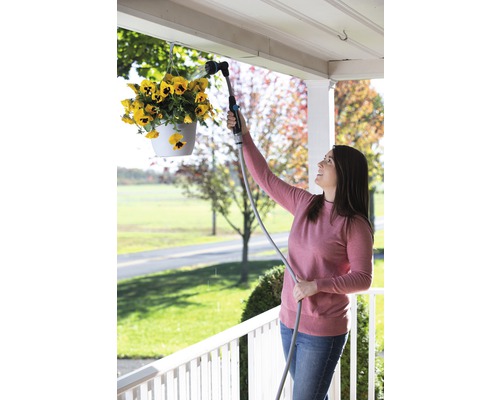 Žena zalévá visící květiny zahradní sprchou.