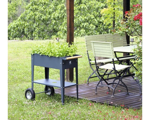 Zahradní scéna s kovovým vozíkem na bylinky, zahradním stolem a zahradní lavicí na dřevěné terase.