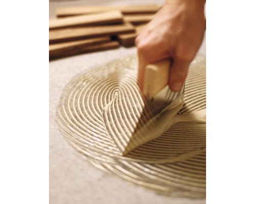 Řemeslník rozděluje lepidlo špachtlí pro pokládku dřevěných výrobků.