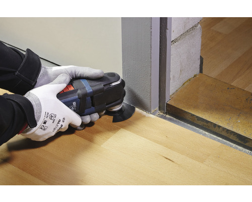 Operátor používá multifunkční nástroj k řezání na dřevěné podlaze