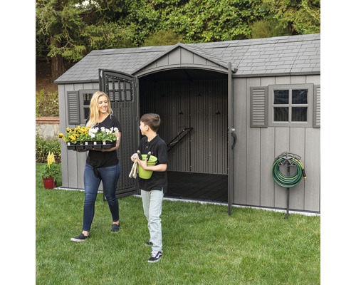 Zahradní scéna s kůlnou na nářadí, ženou a chlapcem nesoucím zahradní potřeby