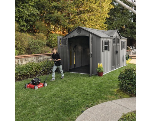 Zahradní scéna s kůlnou na nářadí a osobou sekající trávník