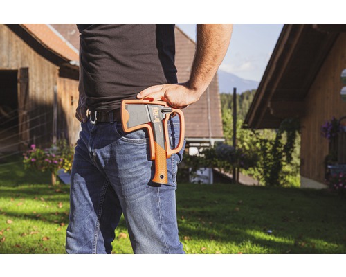 Osoba se sekerou v pouzdře na opasku ve venkovním prostředí.