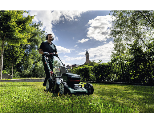 Muž seká trávník pomocí akumulátorové sekačky Metabo na zahradě.