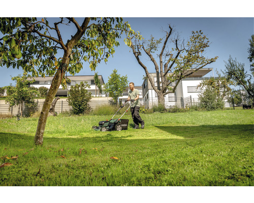 Muž seká trávník se sekačkou na zahradě.