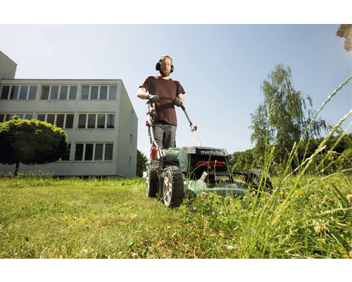 Muž se sluchátky na uších seká trávník sekačkou Metabo
