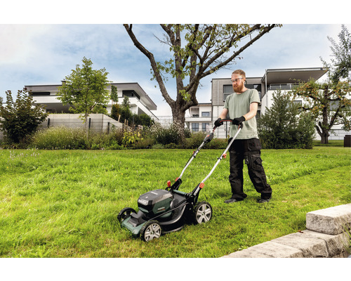 Muž seče trávník akumulátorovou sekačkou na zahradě.