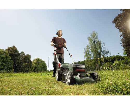 Muž seče trávník sekačkou na trávu Metabo na zahradě.