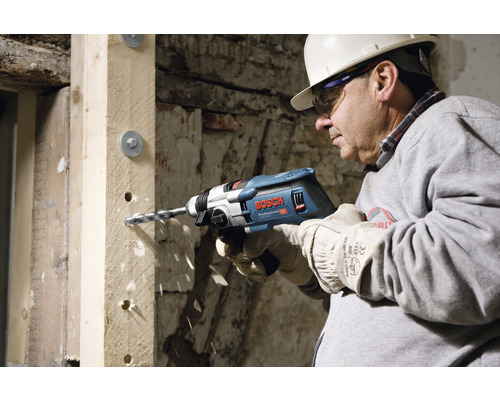 Řemeslník vrtá otvor do dřevěného trámu pomocí příklepové vrtačky Bosch