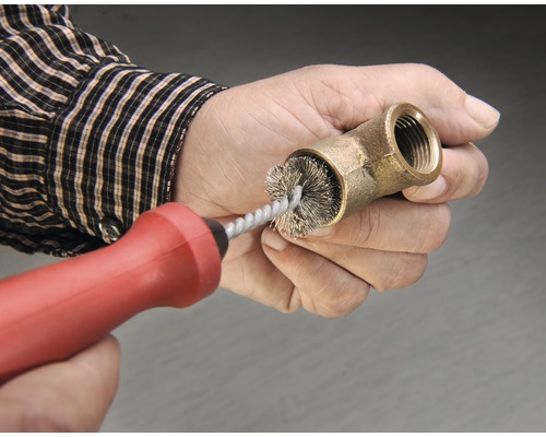 Osoba čistí mosaznou trubkovou tvarovku drátěným kartáčem.