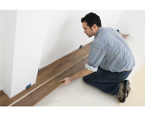 Muž pokládá laminátovou podlahu v interiéru s distančními podložkami.