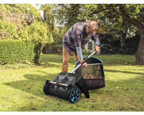 Muž používá zametací stroj na trávník na zahradě ke sběru listí.