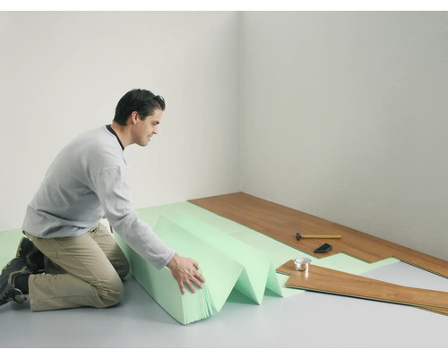 Muž pokládá laminátovou podlahu s kročejovou izolací