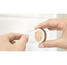Ruka drží kulatý magnetický zámek a odstraňuje ochrannou fólii z lepicí podložky.