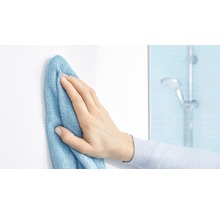 Ruka utírá bílý povrch čisticím hadříkem v koupelně.
