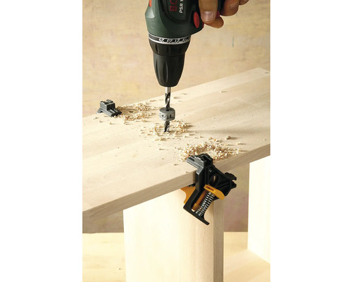 Vrtačka vrtá do dřevěné desky upevněné pomocí úhelníkové svorky.