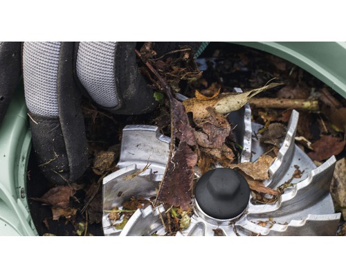 Detail řezacího mechanismu zahradního drtiče se zahradními rukavicemi a listím