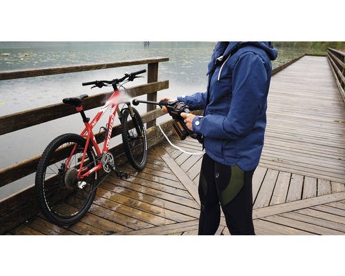 Osoba čistí kolo pomocí přenosné tlakové myčky na dřevěném mostě poblíž vodní plochy.