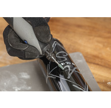 Osoba gravíruje tmavou láhev pomocí nástroje Dremel.