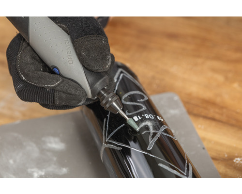 Osoba gravíruje tmavou láhev pomocí nástroje Dremel.