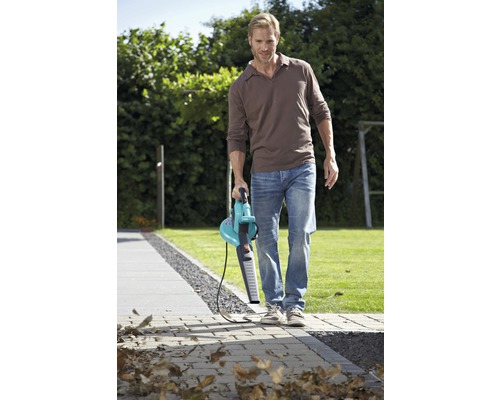 Muž čistí zahradní chodník pomocí fukaru na listí.