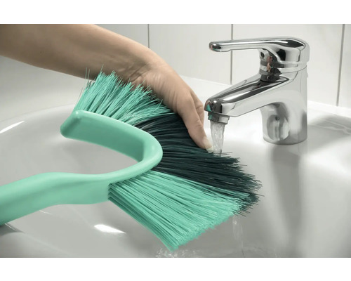 Ruka pod kohoutkem s čisticím kartáčem v umyvadle