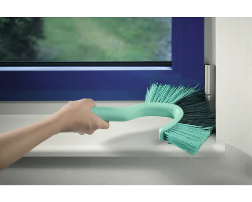 Ruka čistí rám okna pomocí kartáče na okenní rámy.