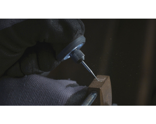 Detailní záběr ruky s ochrannou rukavicí, která ryje tvar do kovového předmětu pomocí rycího hrotu