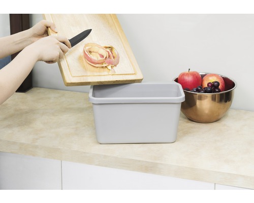 "Osoba vysypává jablečné slupky z dřevěného prkénka do odpadkového koše