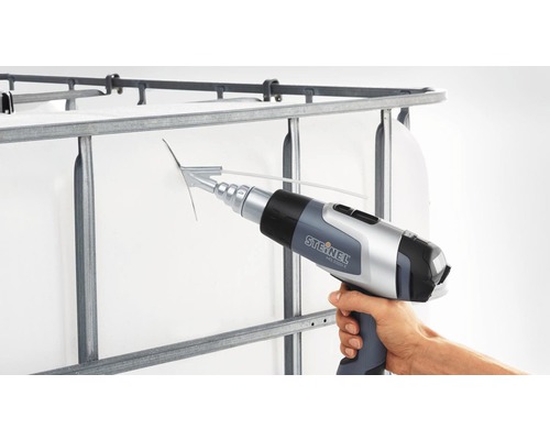 Ruka drží horkovzdušnou pistoli Steinel na mřížce velkoobjemového kontejneru.