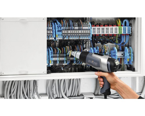 Elektrikář pracuje s horkovzdušnou pistolí na rozvodné skříni