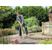 Muž odstraňuje plevel elektrickým odstraňovačem spár na dlážděném povrchu v zahradě.