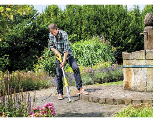 Muž odstraňuje plevel elektrickým odstraňovačem spár na dlážděném povrchu v zahradě.