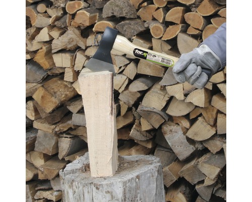 Sekera štípá špalek dřeva před hromadou dřeva