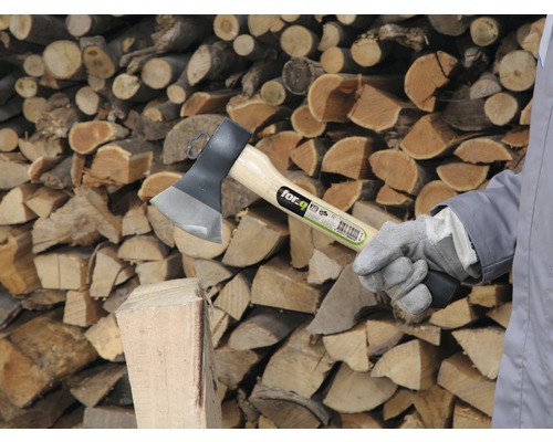 Štípací sekera s kmenem a hromadou dřeva v pozadí