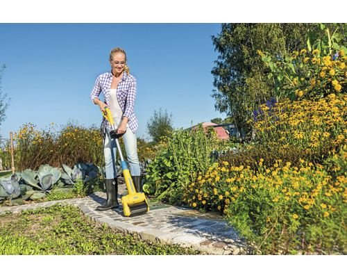 Žena odstraňuje plevel elektrickým kartáčem na spáry na zahradní cestě.
