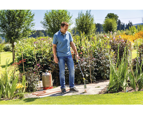 Muž odstraňuje plevel plynovým hořákem na kamenné terase v zahradě.