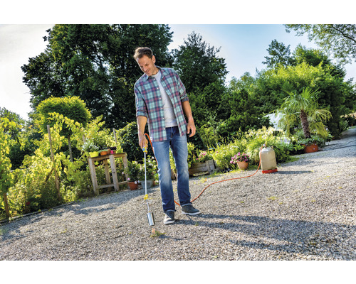 Muž používá plynový hořák k hubení plevele na zahradě.