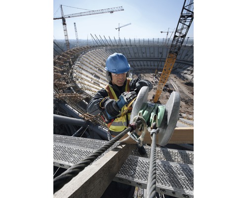 Stavební dělník s ochrannou přilbou a bezpečnostní vestou pracuje s úhlovou bruskou na staveništi.