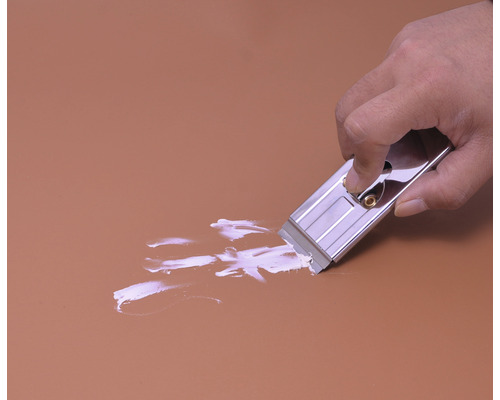 Ruka používá škrabku na sklo k odstranění barvy z povrchu.