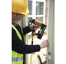 Muž připevňuje okenní rám pneumatickou hřebíkovačkou.