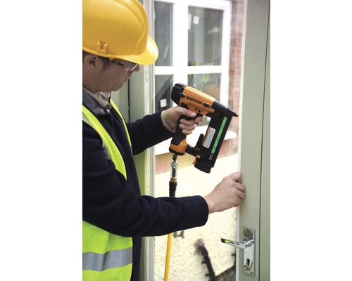 Muž připevňuje okenní rám pneumatickou hřebíkovačkou.