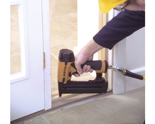 Osoba používá pneumatickou hřebíkovačku Bostitch k připevnění rámu dveří.