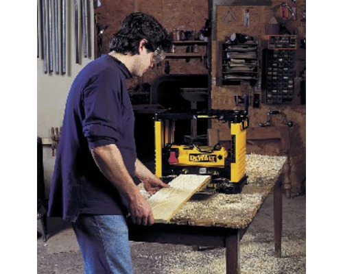 Muž hobluje dřevěnou desku hoblíkem DeWalt na stole.