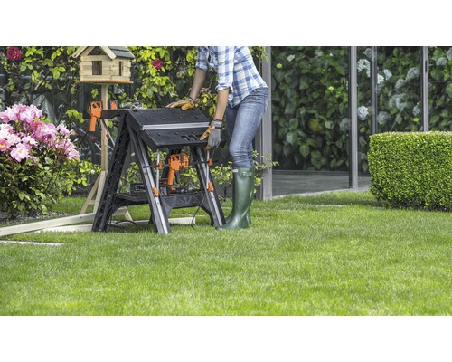 Žena pracuje na skládacím pracovním stole na zahradě.