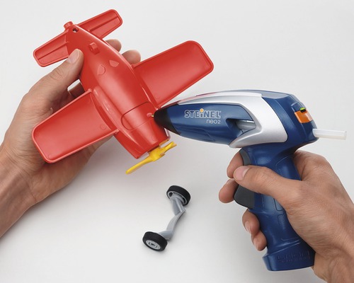 Osoba lepí červené hračkářské letadlo horkovzdušnou pistolí