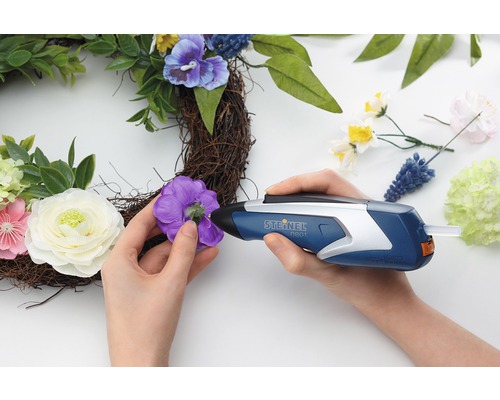 Osoba připevňuje květinu k věnci pomocí tavné pistole.