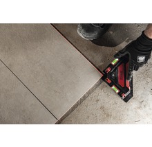 Muž pokládá dlaždice pomocí laserového úhelníku.