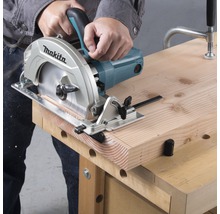 Osoba řeže dřevěnou desku kotoučovou pilou na pracovním stole.